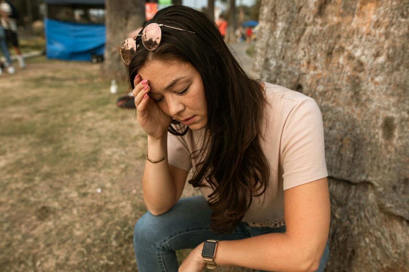 An anxious woman outdoors touching her forehead, showing stress and mental exhaustion.